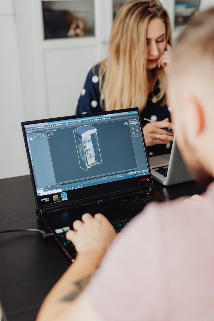 Two colleagues working on laptops indoors, focusing on 3D modeling software.